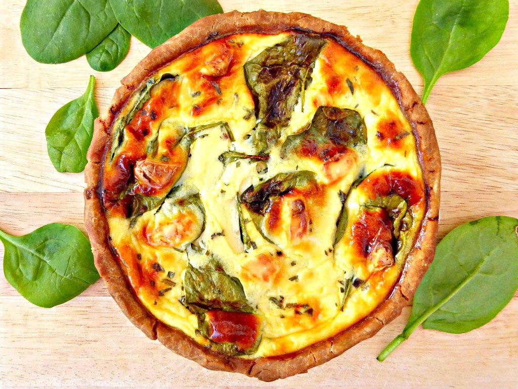 close up image of a round cheese pie on a wooden board with spinach leaves sprinkled around it
