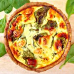 close up image of a round cheese pie on a wooden board with spinach leaves sprinkled around it