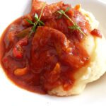 a close up of mash covered with a red stew