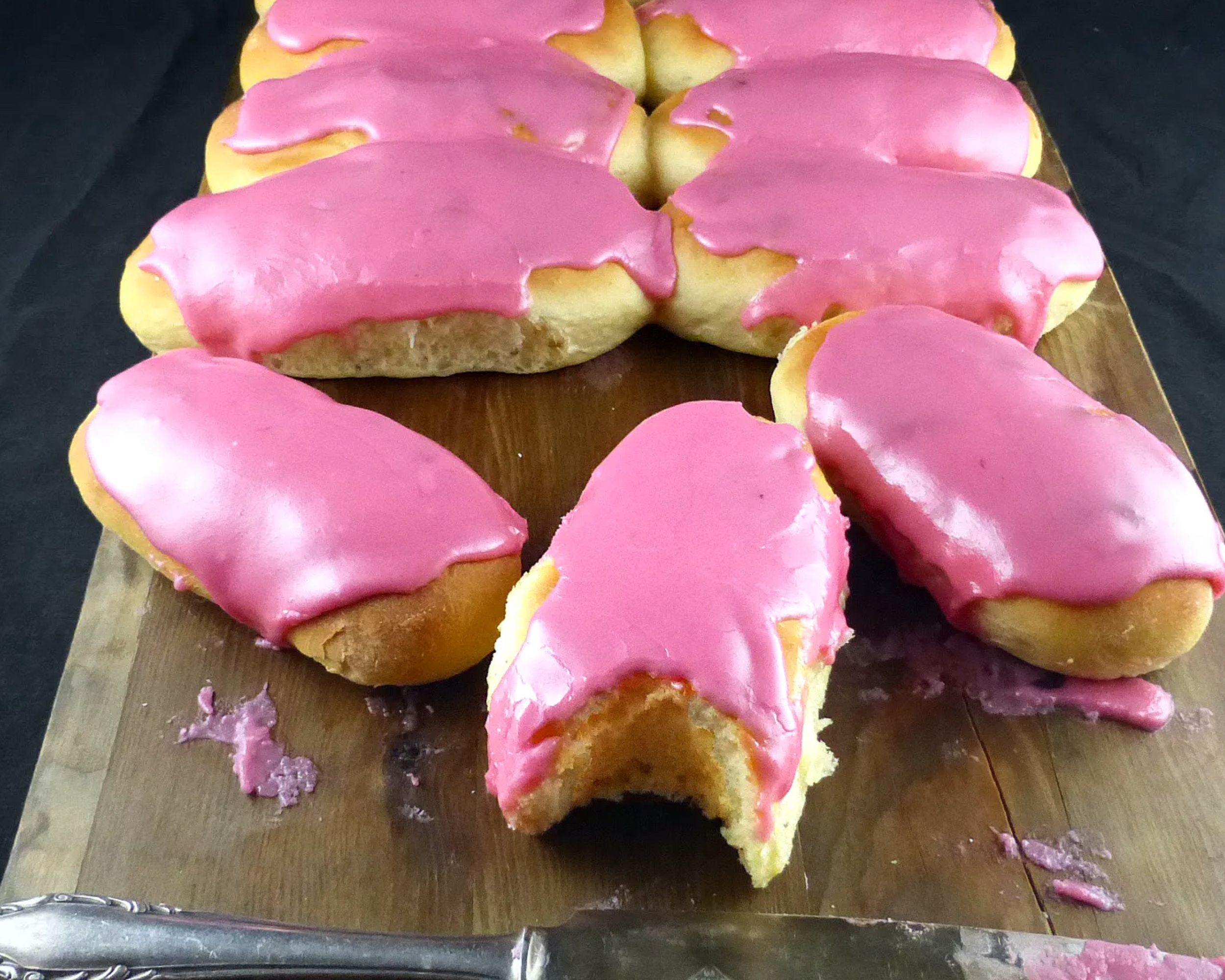pink iced finger buns on a wooden board