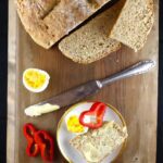 overhead shot of soda bread with a slice on a plate, eggs, and red peppers on a wooden board