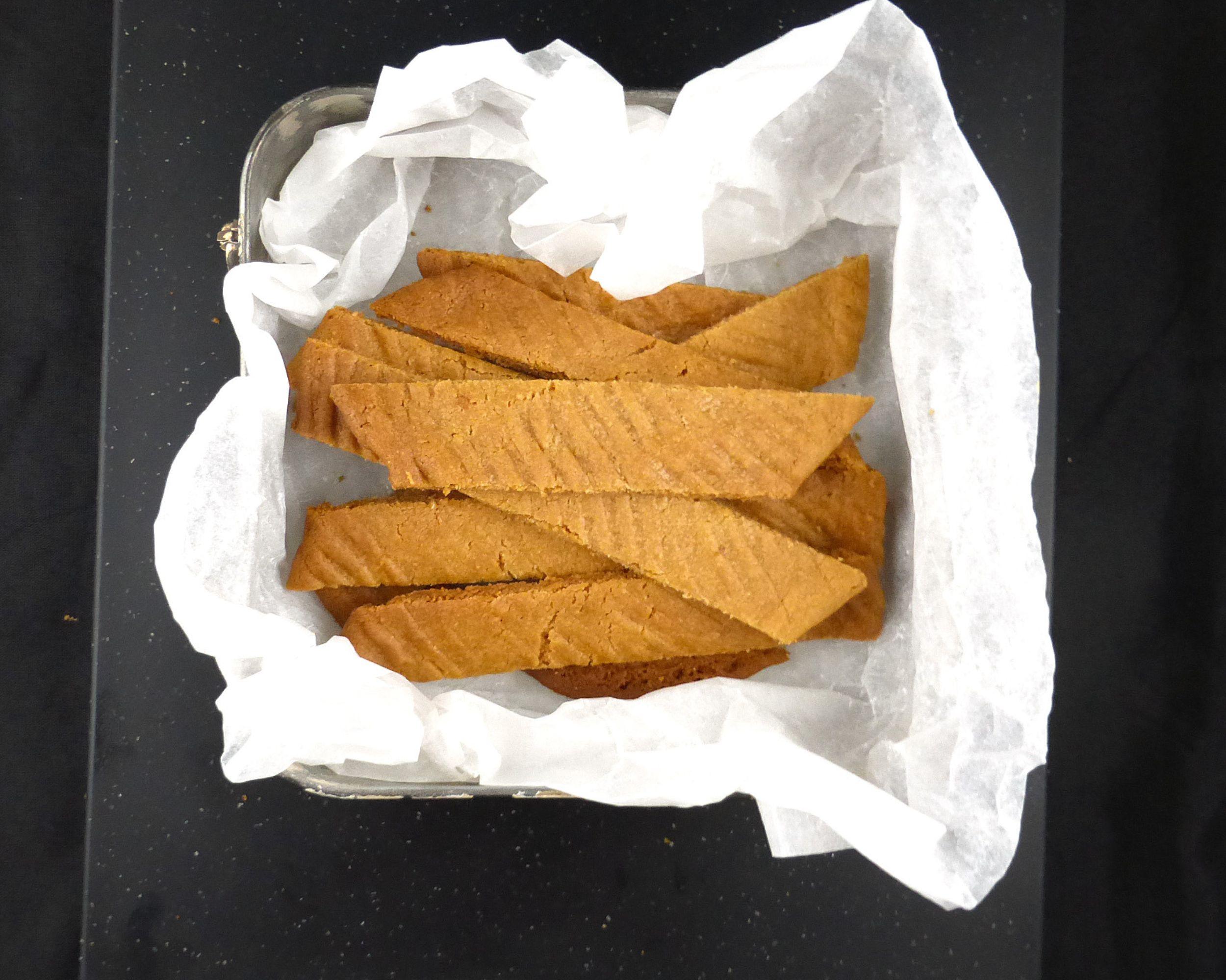 overhead view of toffee cookies in baking paper on a black background