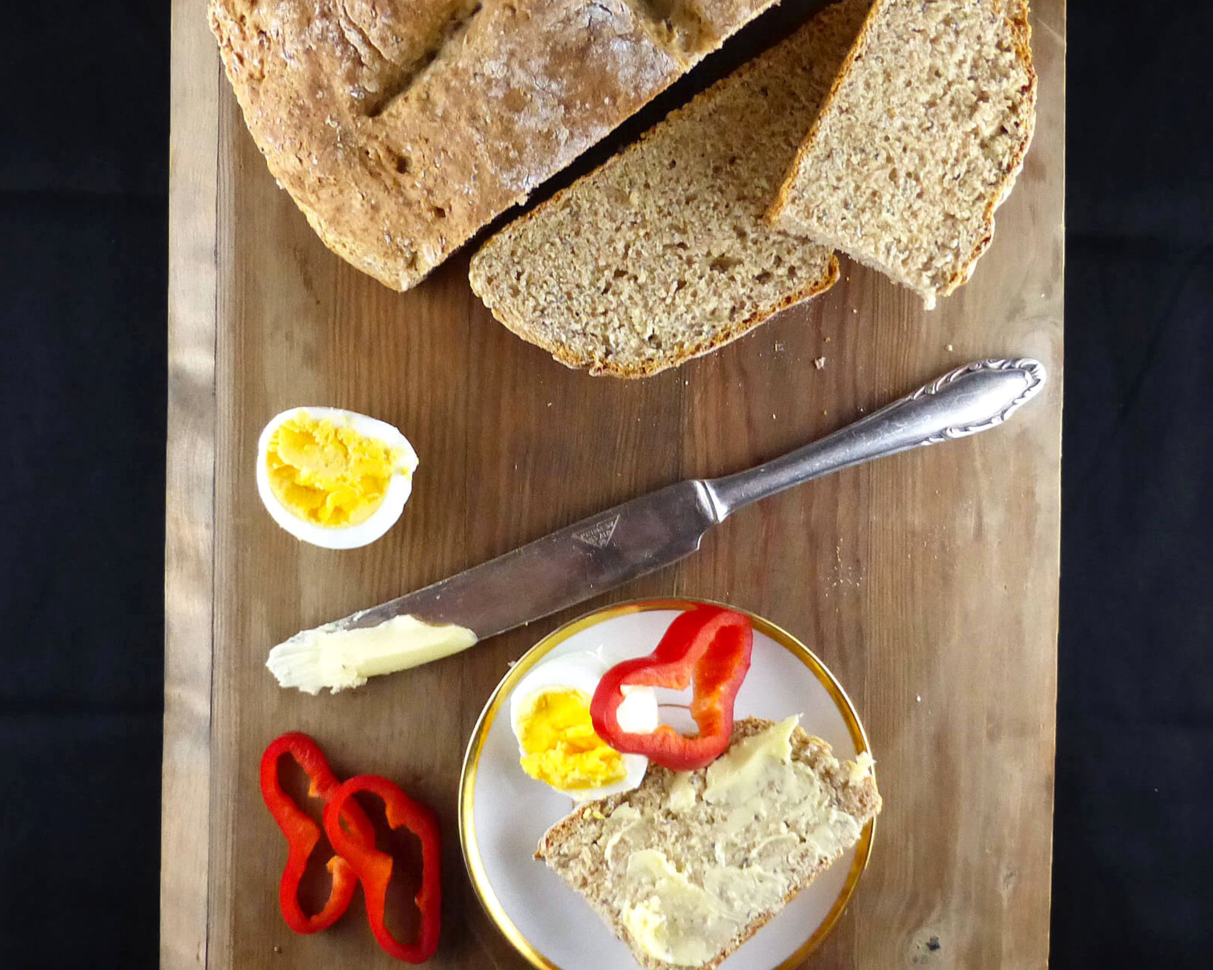 overhead shot of soda bread with a slice on a plate, eggs, and red peppers on a wooden board