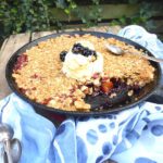 picture of an apple and blackberry dessert in a skillet with a blue scarf and tablespoons by the side