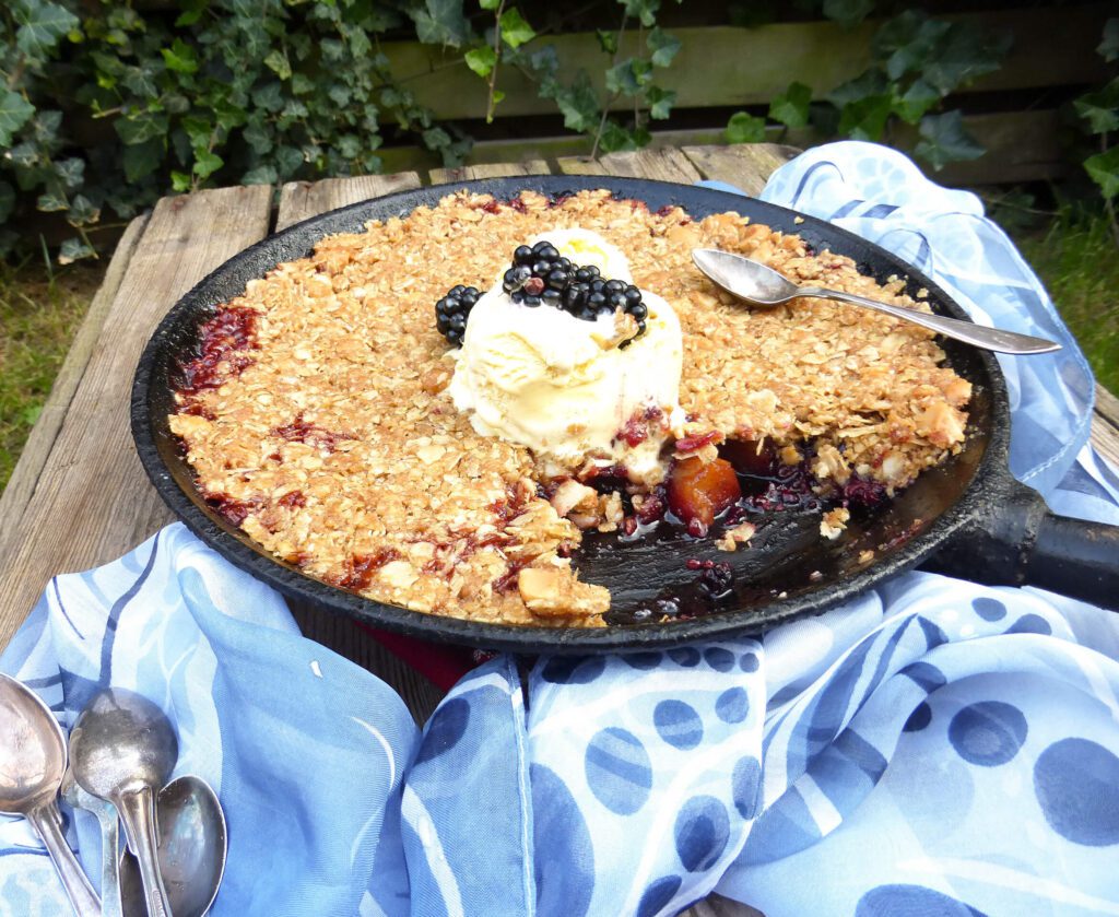 picture of an apple and blackberry dessert in a skillet with a blue scarf and tablespoons by the side