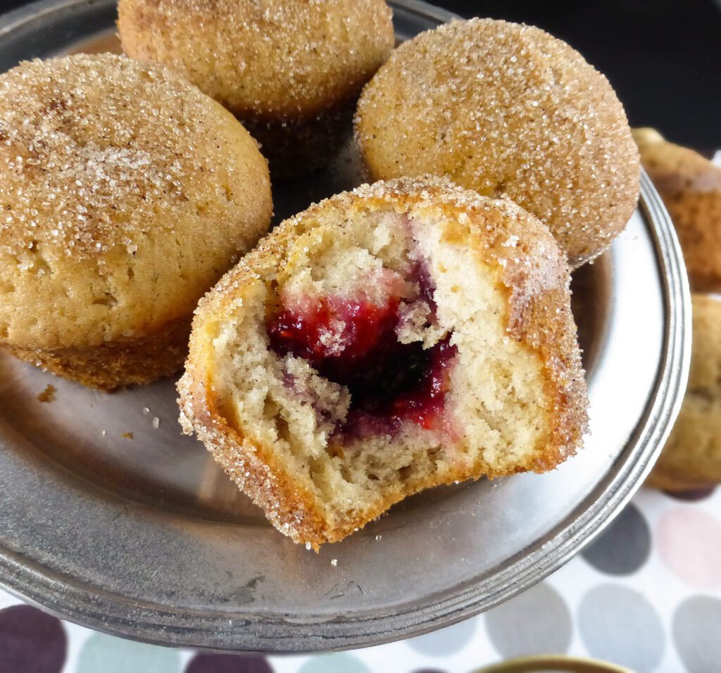 a close up of a doughnut muffin with a bite taken out and raspberry jam showing in the middle
