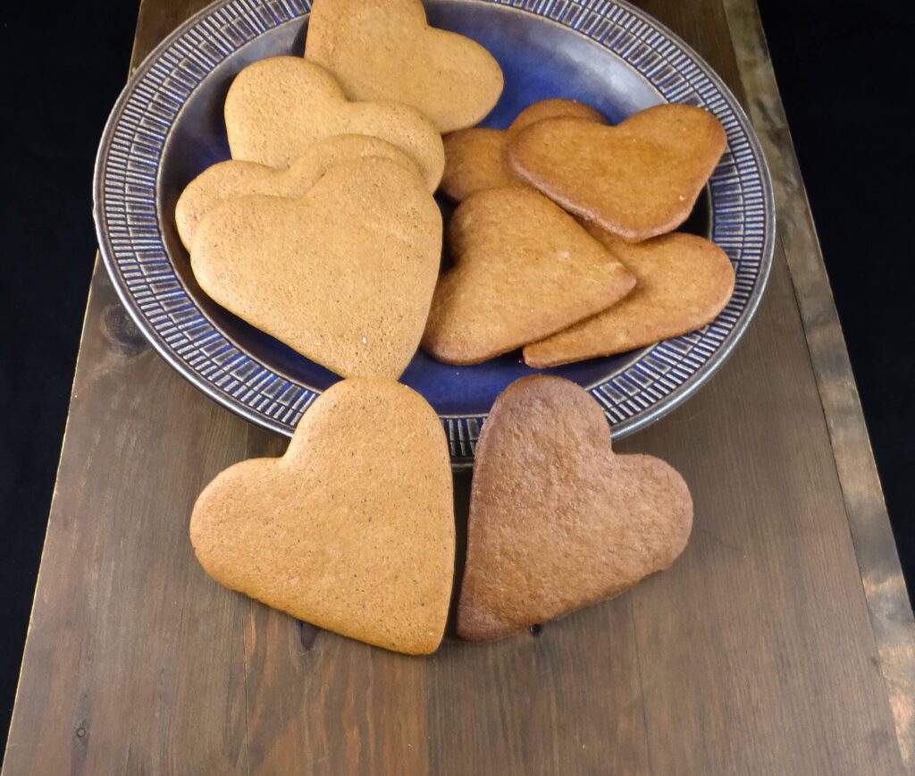 heart-shaped Swedish pepparkakor on a blue plate on top of a wooden board