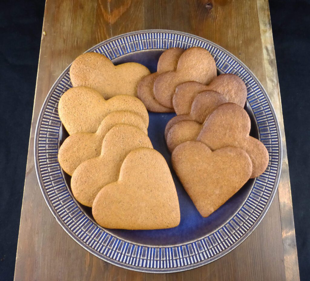 heart-shaped Swedish pepparkakor on a blue plate on top of a wooden board