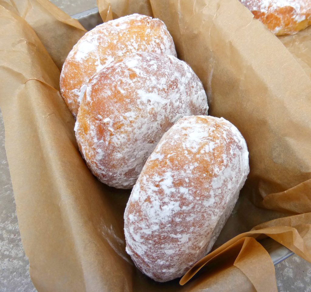 three doughnuts lying in a baking tin covered with brown paper