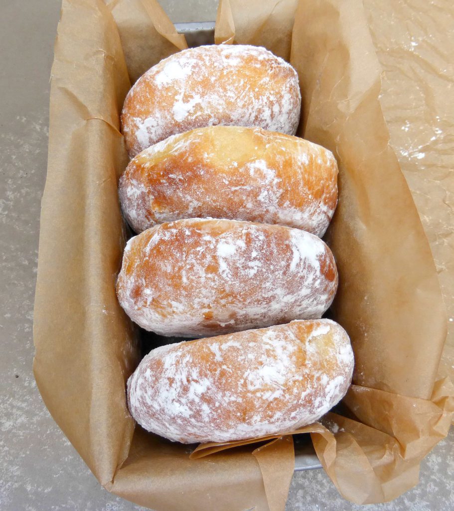 four Nutella doughnuts in a vertical row on brown baking paper