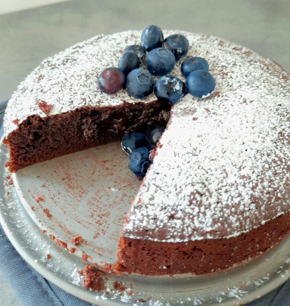 picture of a chocolate cake with a slice missing and blueberries on top