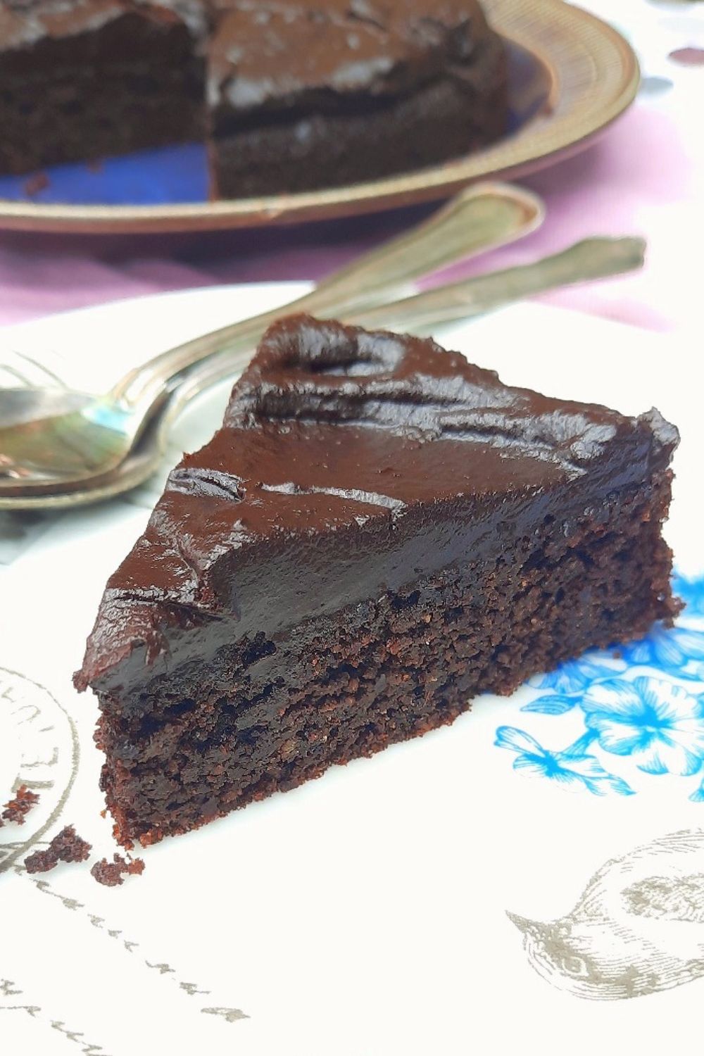 Slice of healthy chocolate cake with fudgy date chocolate frosting, naturally sweetened with maple syrup, on a white plate