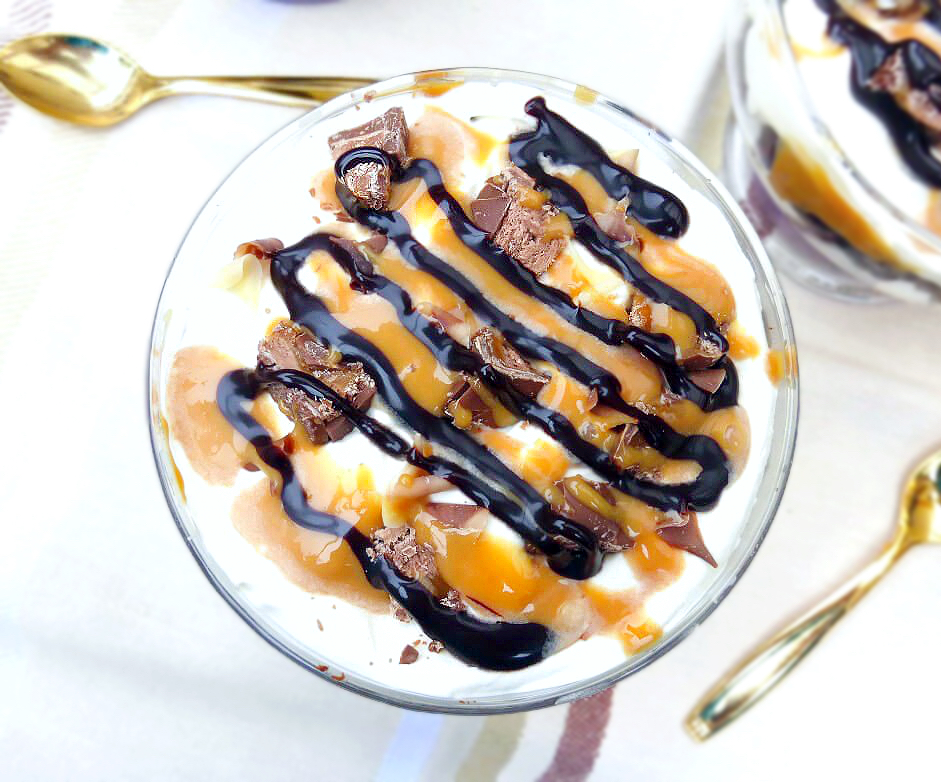 Overhead view of a bowl of caramel, cream and cake trifle with drizzles of chocolate and caramel and sprinkles of chopped Mars Bar