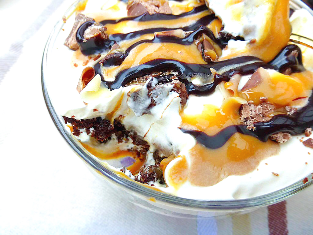 Close up view of a bowl of caramel, cream and cake trifle with drizzles of chocolate and caramel and sprinkles of chopped Mars Bar