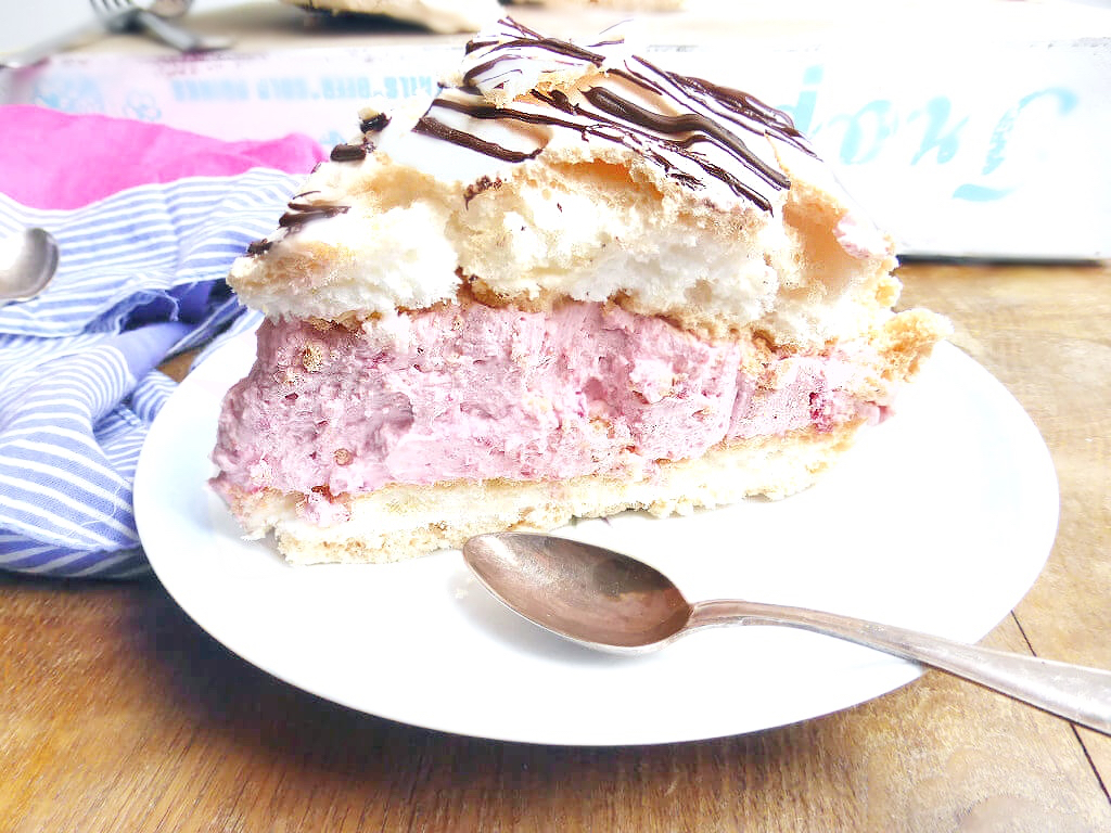 close up view of a meringue filled with raspberry cream filling on a small place with a spoon on a wooden table