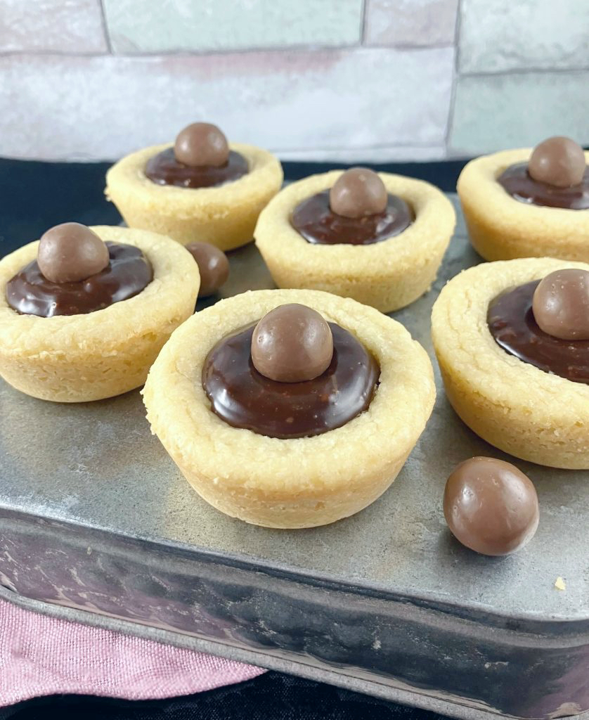 Cookie cups filled with Nutella ganache on a silver blue box with a colorful tile affect behind