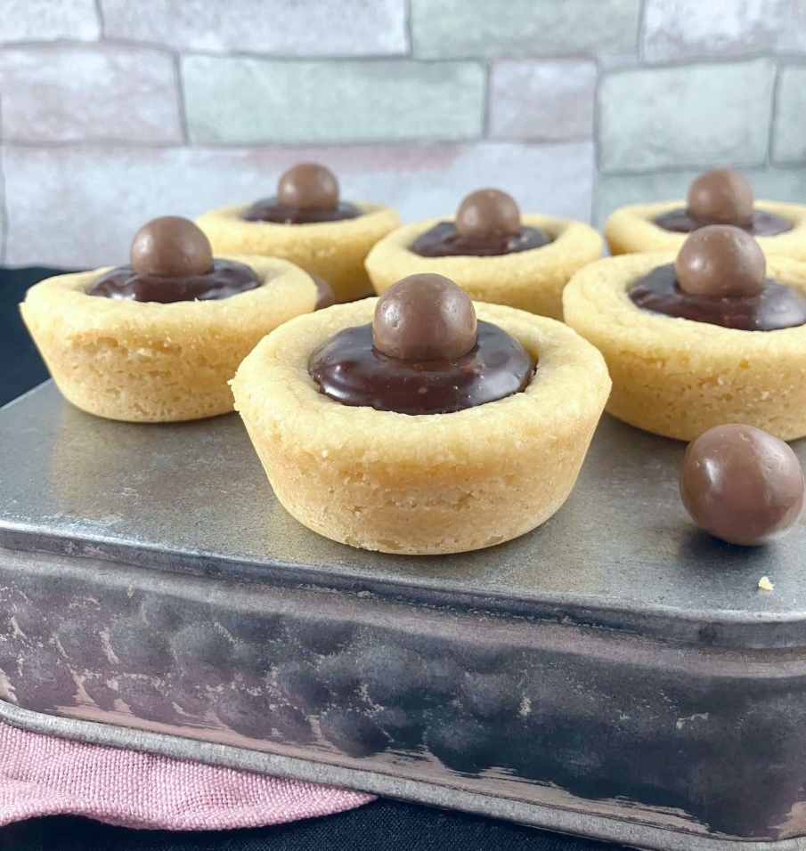 Cookie cups filled with Nutella ganache on a silver blue box with a colorful tile affect behind