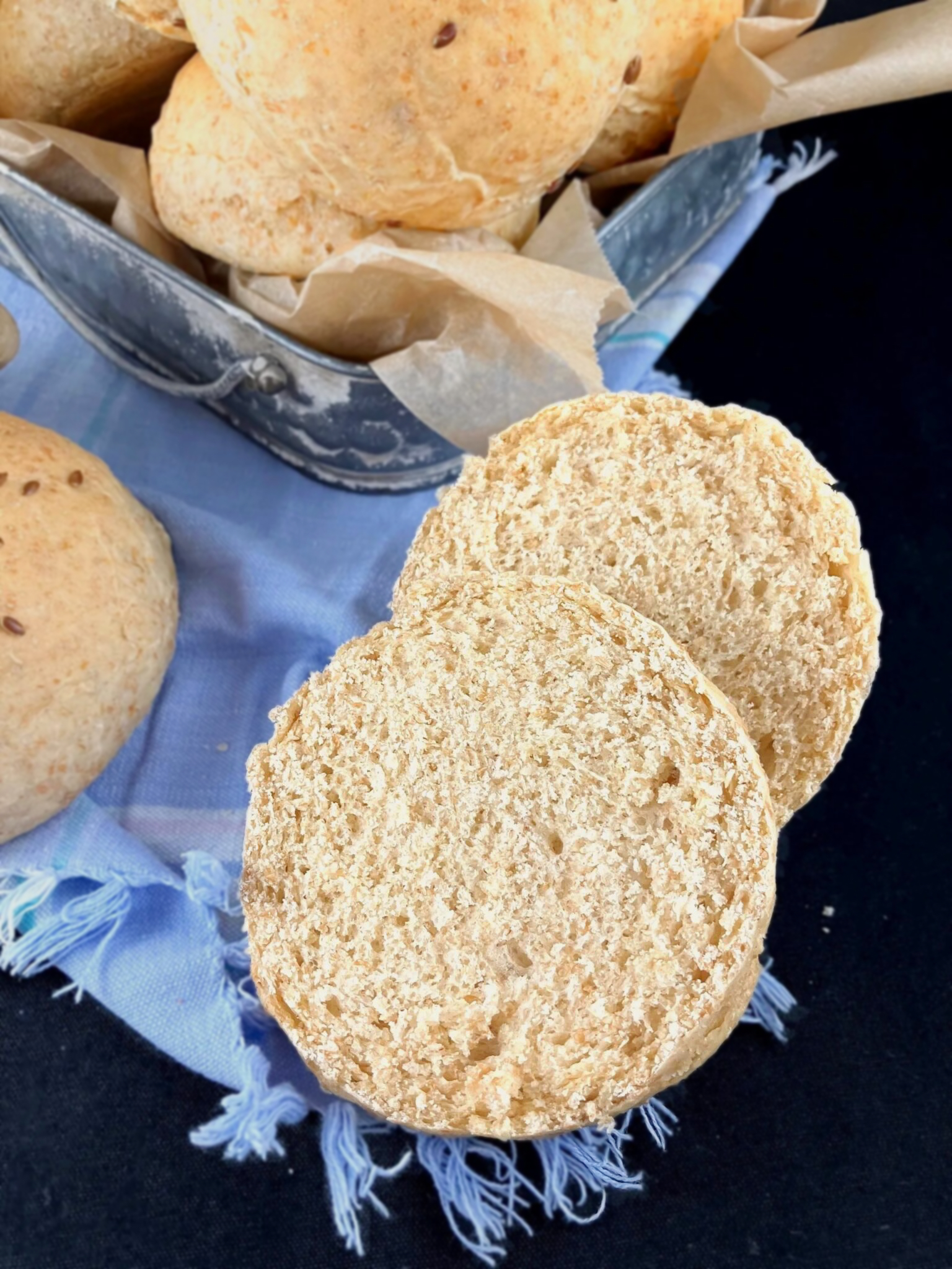 Wholegrain spelt bread buns made with cooked oats on a blue cloth with a dark background.