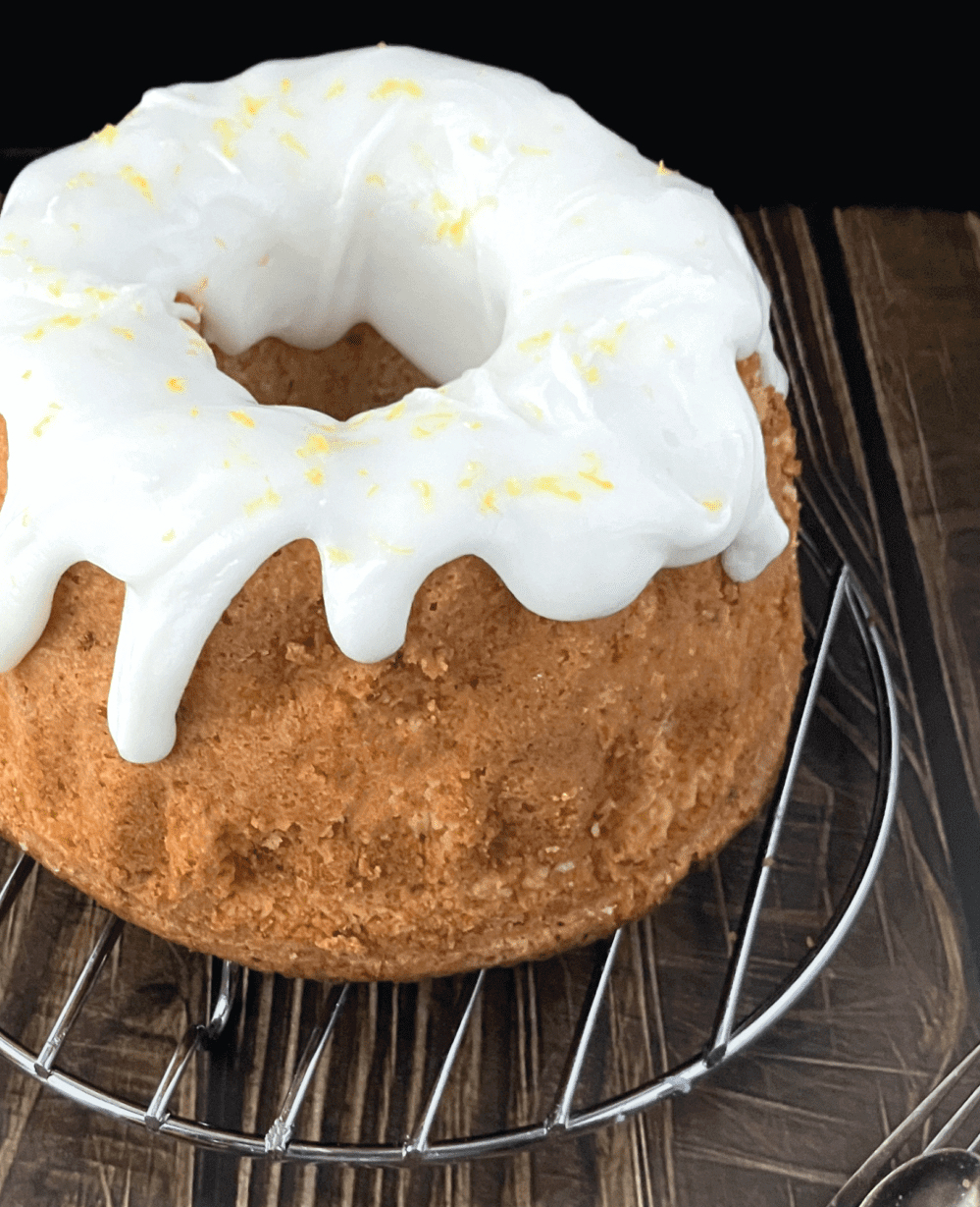 whole lemon and cottage cheese spelt bunt cake side view on a wire rack on top of a wooden affect board