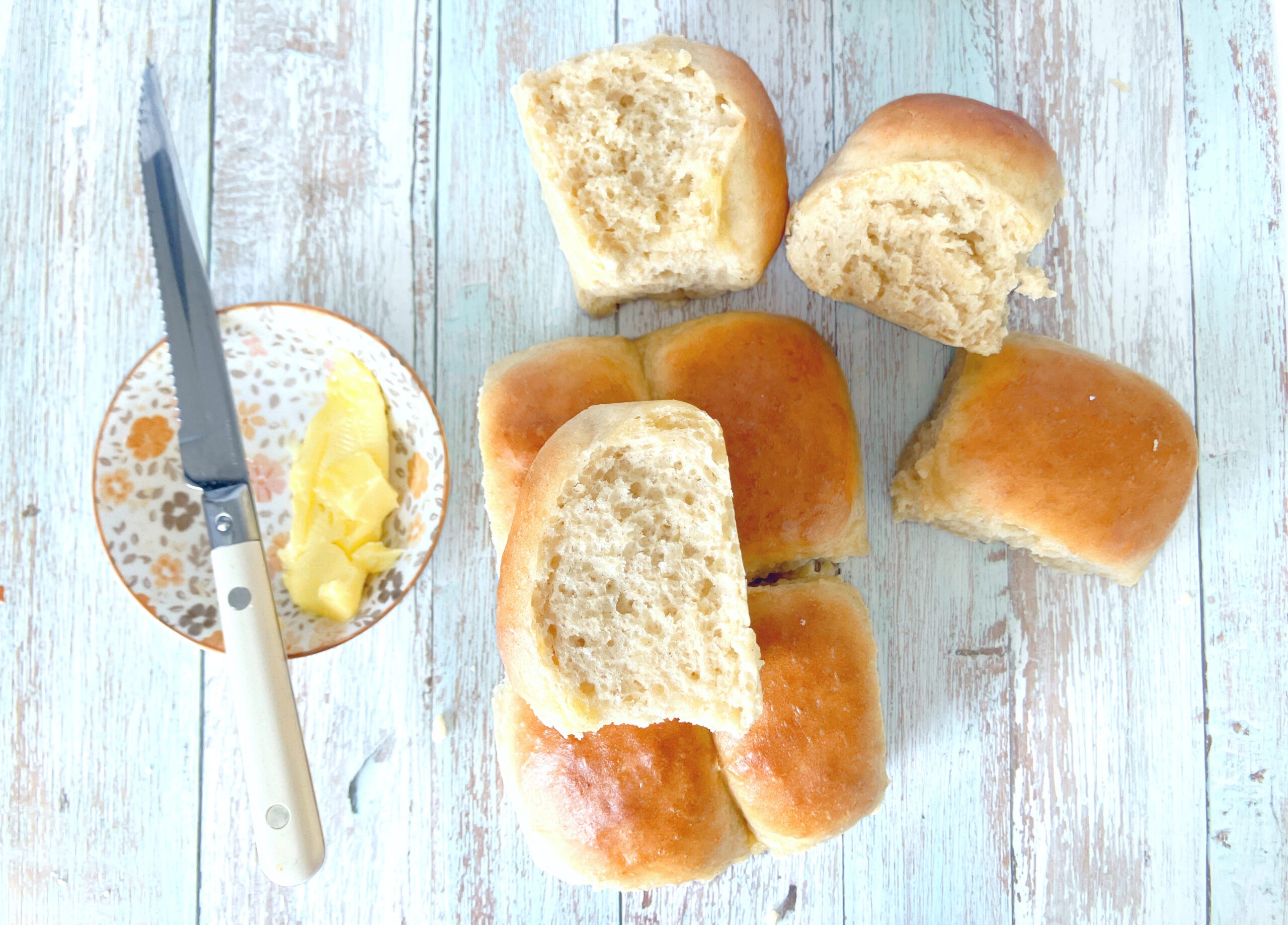 One Hour Spelt Dinner Rolls - small bread buns on a pale blue surface with a bowl of butter and a knife