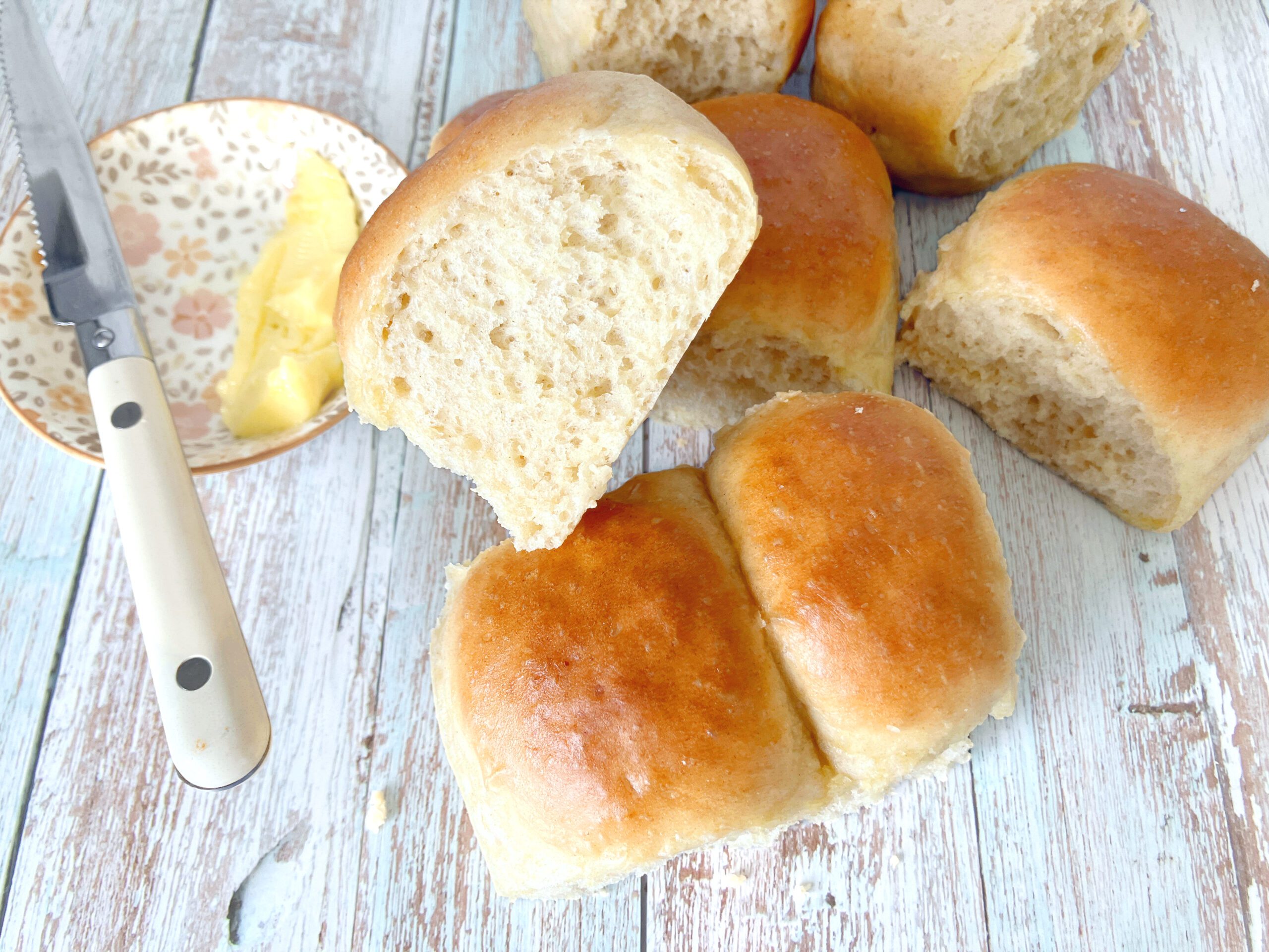 One Hour Spelt Dinner Rolls - small bread buns on a pale blue surface with a bowl of butter and a knife