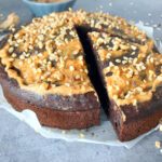 Side view picture of a lighter brownie cake with peanut butter and cottage cheese topped with a light peanut butter frosting and chopped hazelnuts