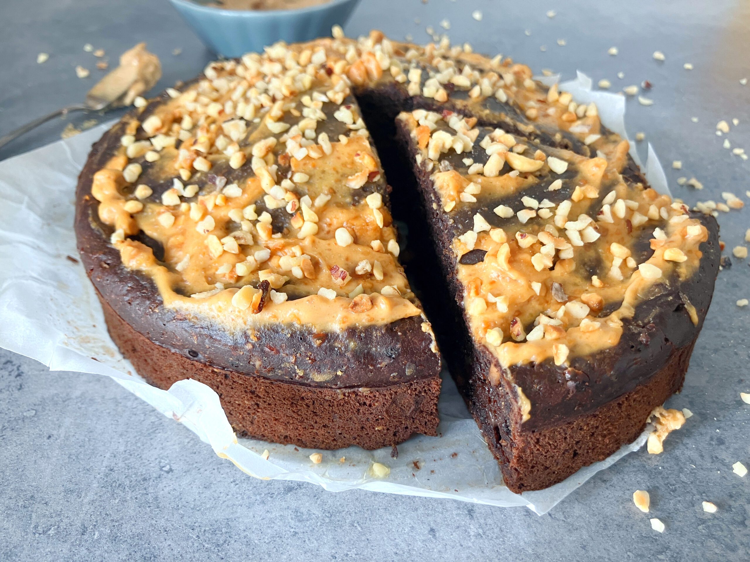 Side view picture of a lighter brownie cake with peanut butter and cottage cheese topped with a light peanut butter frosting and chopped hazelnuts