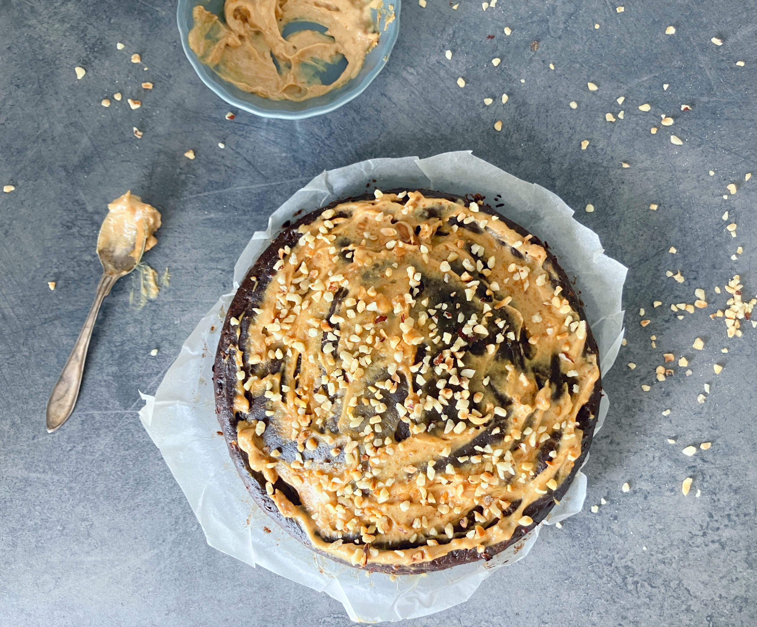 Overhead view picture of a lighter brownie cake with peanut butter and cottage cheese topped with a light peanut butter frosting and chopped hazelnuts
