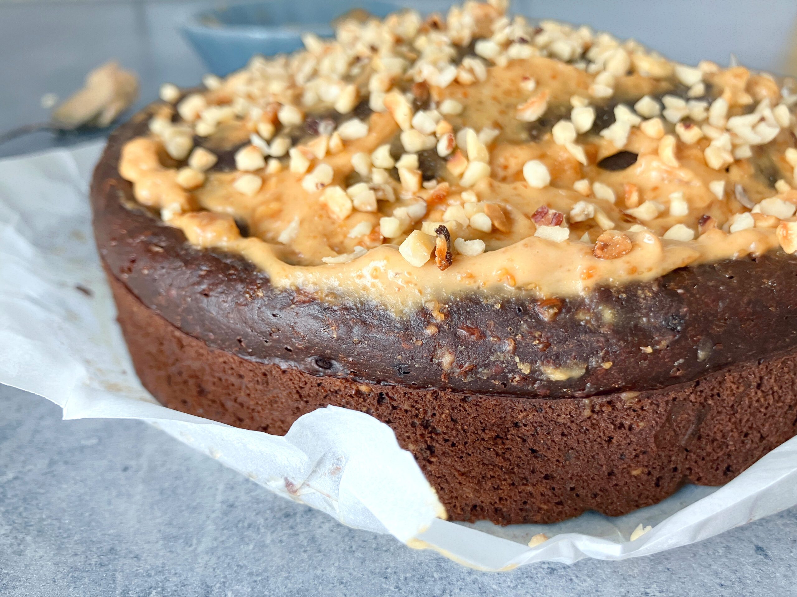 Side view picture of a lighter brownie cake with peanut butter and cottage cheese topped with a light peanut butter frosting and chopped hazelnuts
