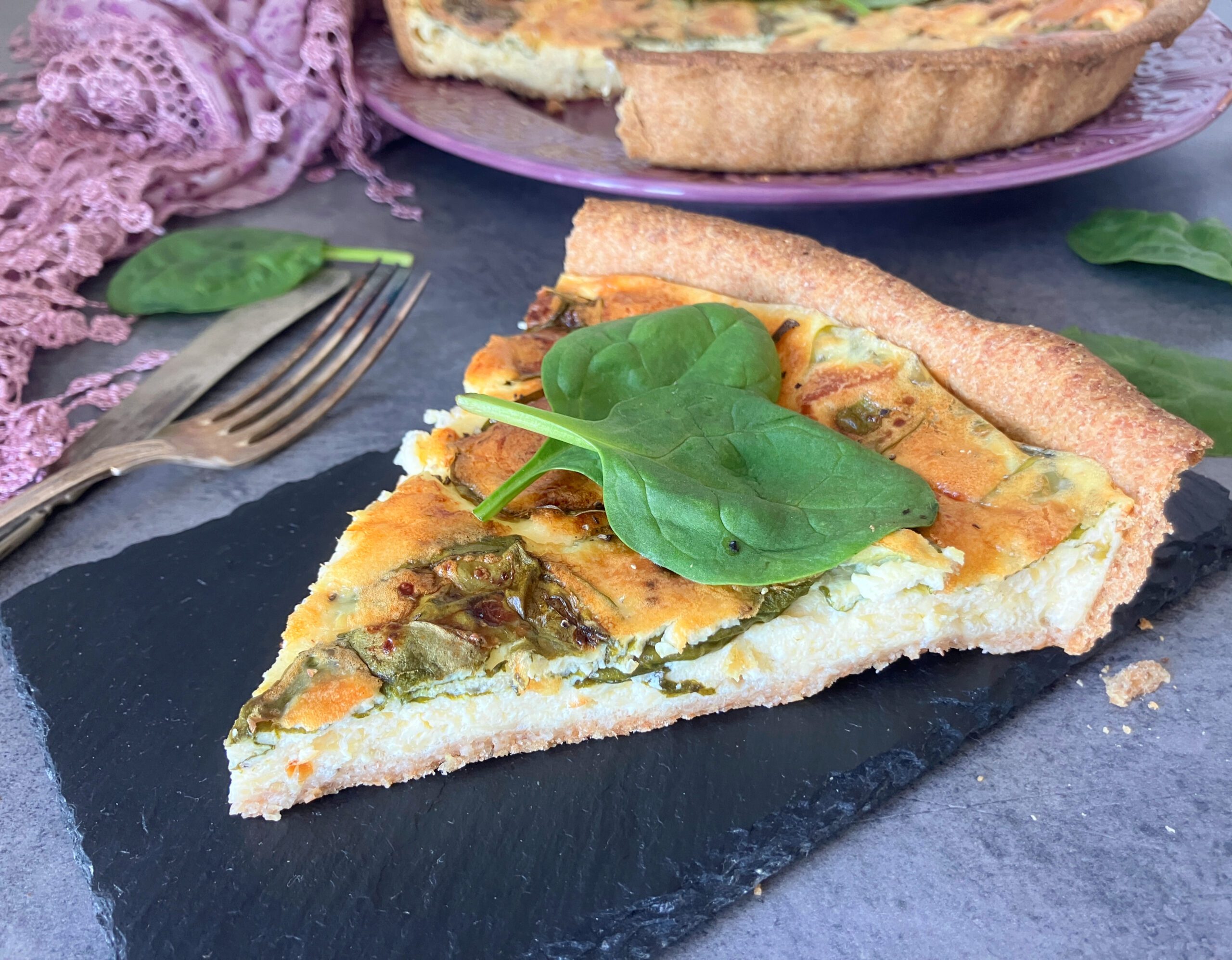 Close up shot of a slice of spelt flour and olive oil crust quiche filled with cottage cheese and Greek yoghurt. With spinach on top