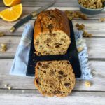 Side view of a dried mulberry tea loaf with a slice on a plate with a cup of tea and oranges