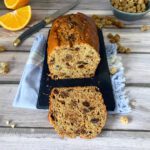 Overhead shot of a dried mulberry tea loaf with a slice on a plate with a cup of tea and oranges